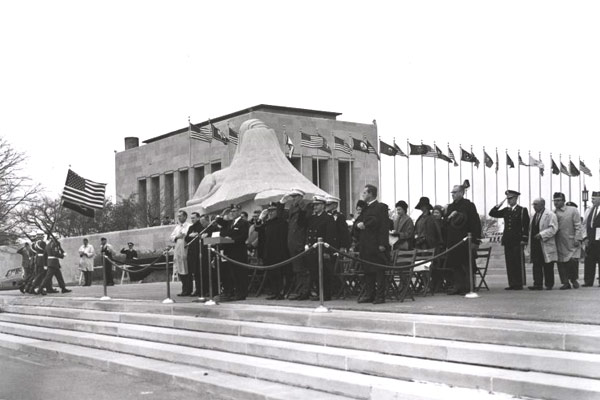 Black-and-white image of the 'Memory' sphinx and Exhibit Hall, surrounded by flags — representing solemn memorial settings often mirrored in local Veterans Day events.